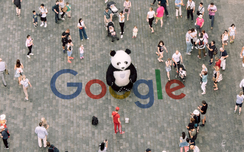 A panda standing in a crowded public space, and the Google logo has been painted on the cobblestones beneath its feet