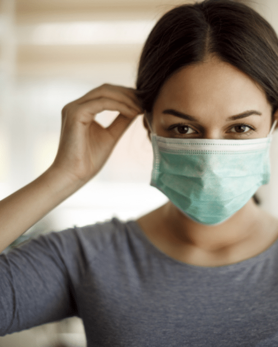 A woman in casual clothes putting on a surgical mask