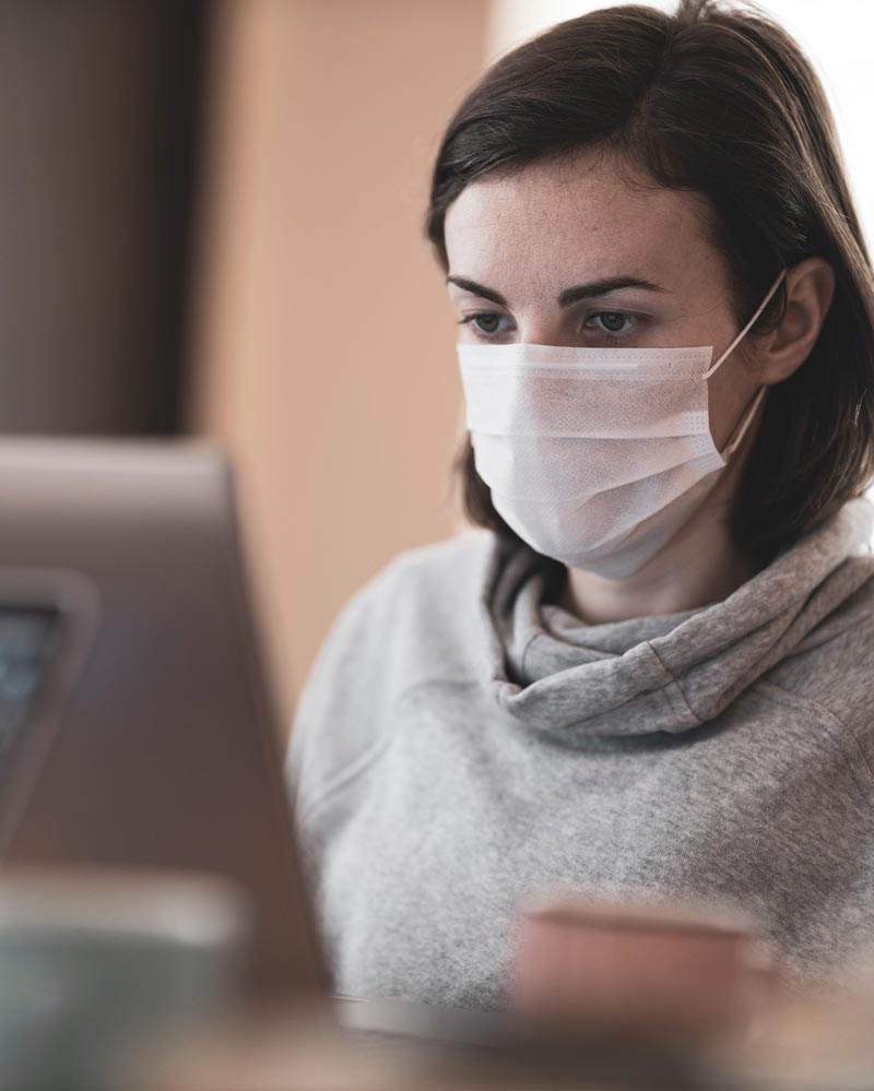 A woman in a facemask looking at a computer screen