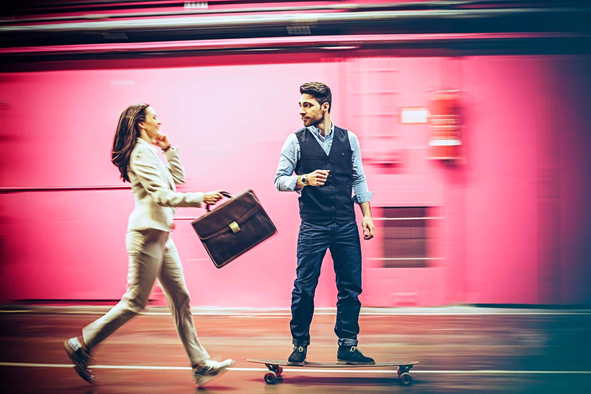 A well dressed man on a skateboard passing a woman who is hurrying with a briefcase and is on the phone