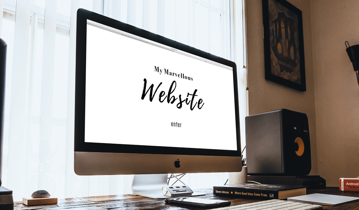 An iMac on a desk displaying a screen reading "My Marvellous Website" and "enter