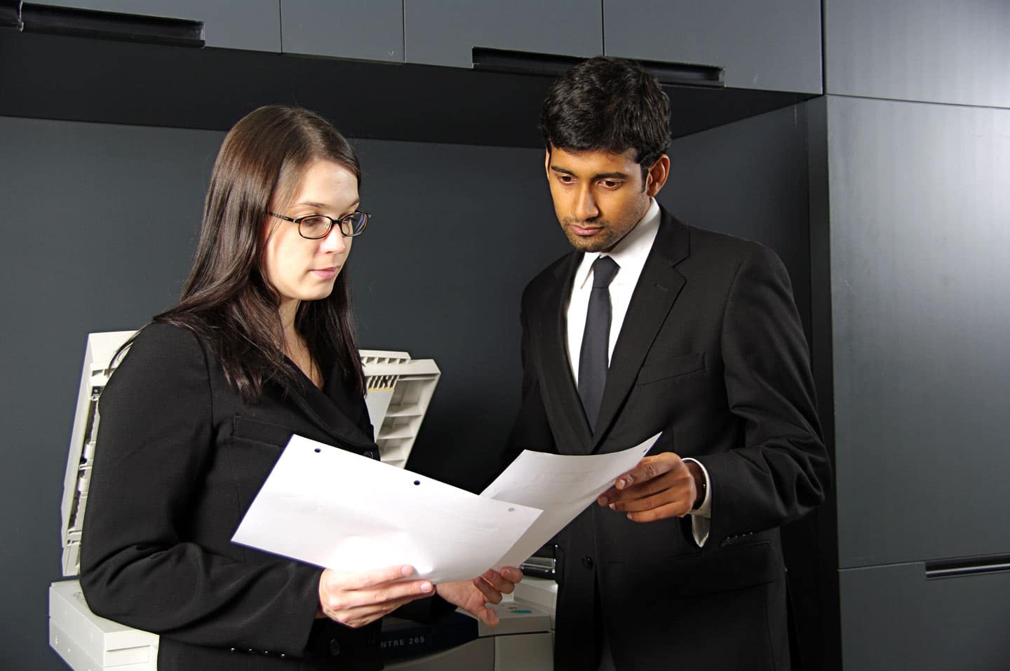 An obviously posed photo of two business type people in front of a photocopier intently looking at a document