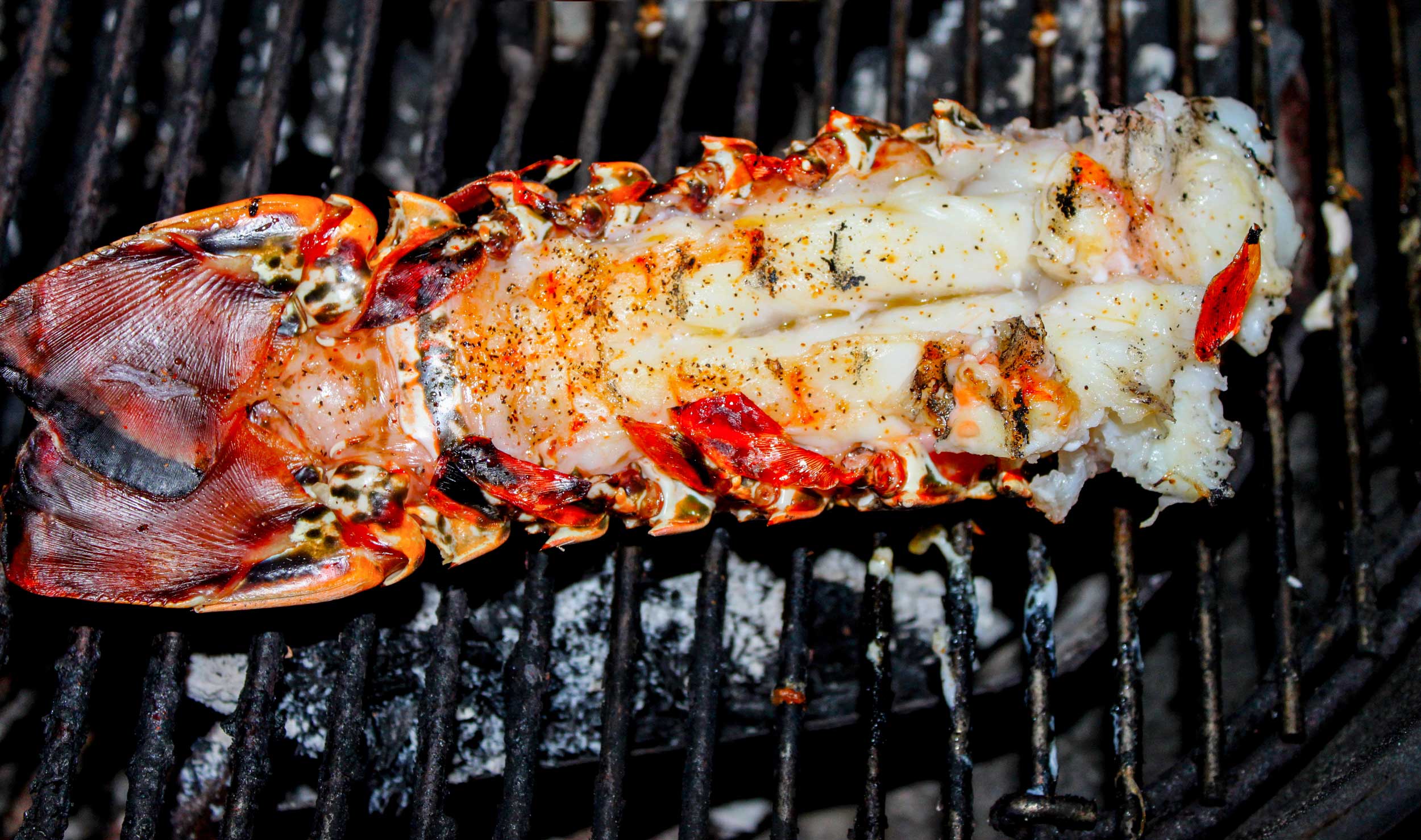 A seasoned lobster tail cooking on a barbeque grill