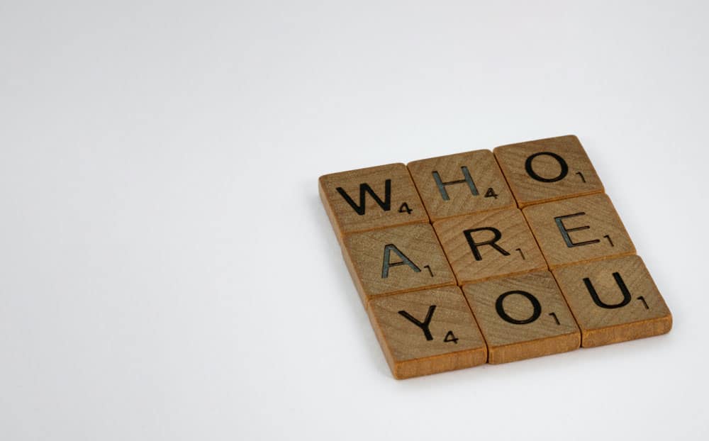 A 3x3 square of scrabble tiles spelling out the words WHO ARE YOU