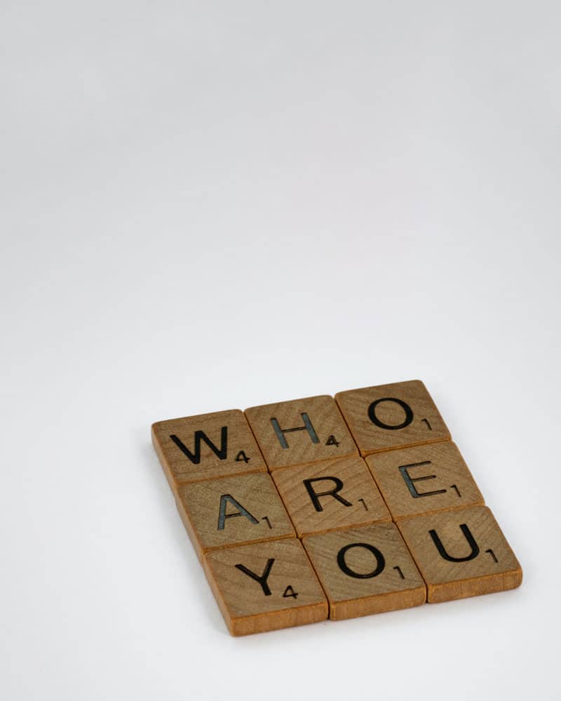 A 3x3 square of scrabble tiles spelling out the words WHO ARE YOU