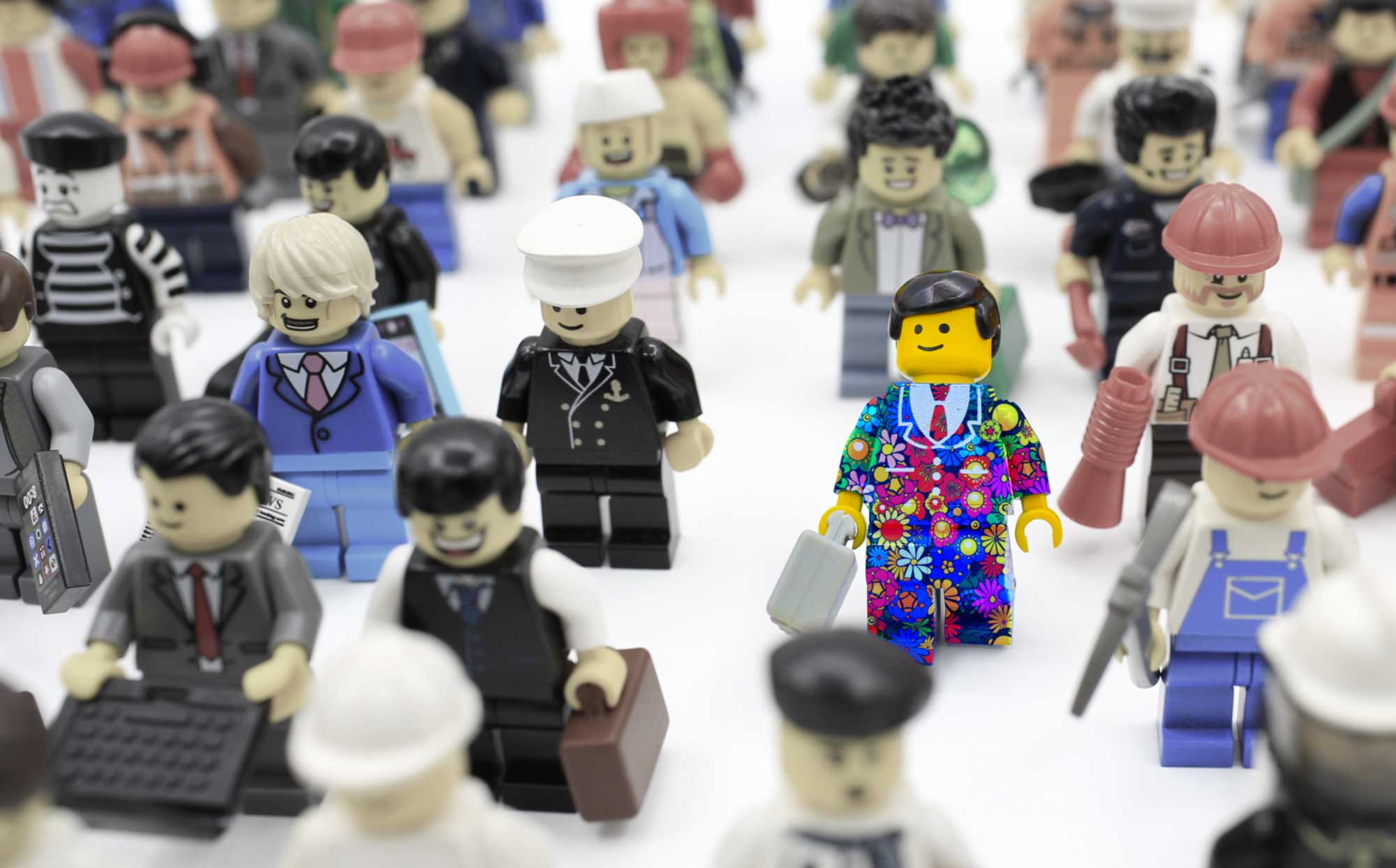 A brightly coloured lego man in a floral suit, standing amongst a crowd of drab lego figures